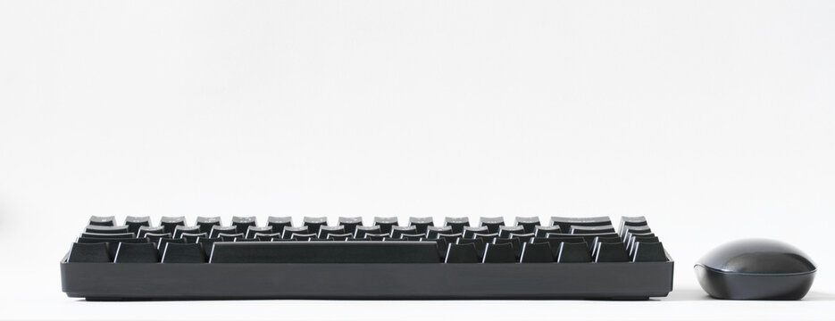 Portable computer keyboard equipped with mechanical switches and a black computer mouse on a white background. Wireless input devices for gadgets. Copy space. Side view.