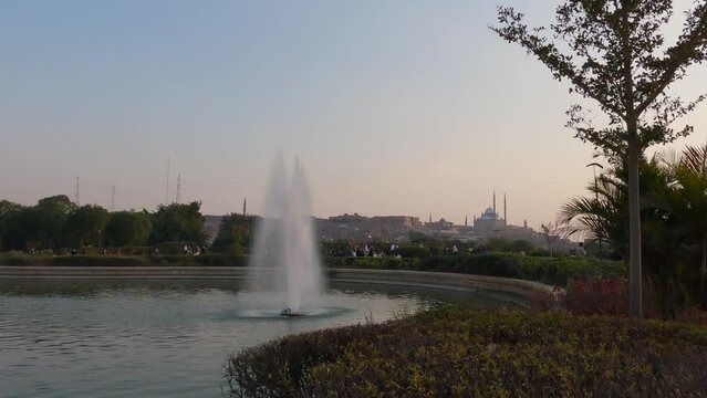 Panning shot of tourists exploring Al Azhar Park with a large water fountain in the foreground