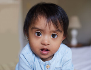 Face, down syndrome baby and bedroom portrait in home alone, looking innocent and cute. Disability,...