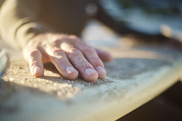 Hand, surfboard and sports with a man surfer cleaning sand from his board after surfing at the...