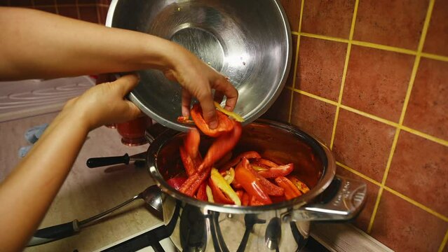 Housewife's hands pour slices of ripe organic sweet bell pepper into a stream with boiling tomato juice, prepares lecho salad for preservation for the winter. Canning vegetables. Food Preservation