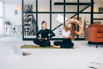 Two young women meditating in lotus pose at home