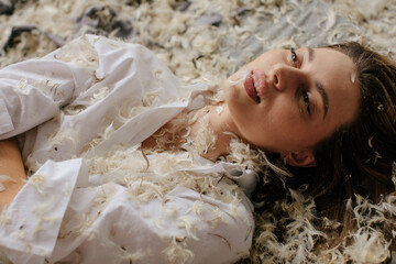 Sensual woman in bed with feathers looking away - dreamy female portrait - fallen angel