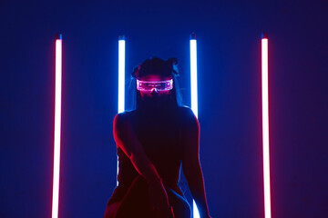Ethnic female in glowing eyeglasses sitting and looking at camera in neon lights