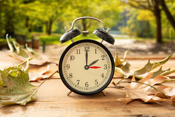 Daylight Saving Time, Fall Back one hour. Black clock on wood, autumn trees background - obrazy, fototapety, plakaty