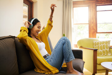 Woman, music and relax with headphones dancing on living room sofa enjoying good vibes at home. Happy female with smile and dance listening to joyful audio streaming, relaxing on a couch at the house