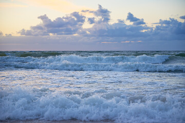 Panoramic view of sea beach with splashing waves against dramatic cloudy sky. Baltic sea coastline at sunset