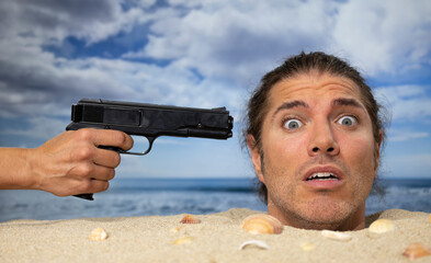 A man buried in sand on beach with gun at him