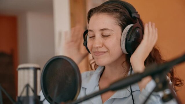 Young woman preparing for a conversation or recording session put on headphones. At her home studio or office desk female host is setting up before video conference with professional microphone