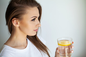 Beautiful young woman drinking fresh water with lemon at home