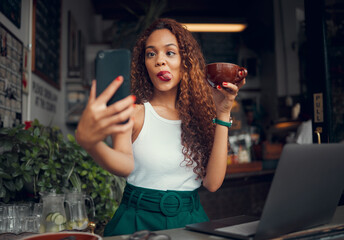 Selfie, coffee shop and funny with a woman customer using a laptop and phone in her local cafe. Silly, face and mobile with a young female posting a photograph on the internet while in a restaurant - obrazy, fototapety, plakaty