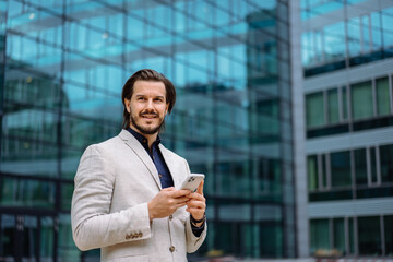 Professional businessman in suit looking at camera while standing on street with mobile phone. App