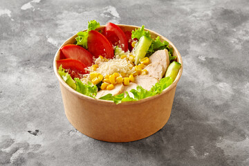 Poke bowl with lettuce, tomatoes, cucumbers, chicken fillet, corn and grated parmesan on gray stone...