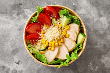 Paper bowl of salad with lettuce, tomatoes, cucumbers, chicken fillet, corn and grated parmesan on...