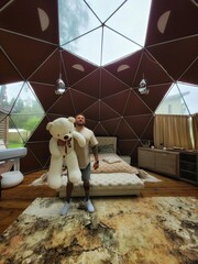hombre en una habitación cúpula con un oso de peluche