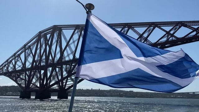 Scottish flag on a blustery day travelling underneath the Forth Bridge, Scotland