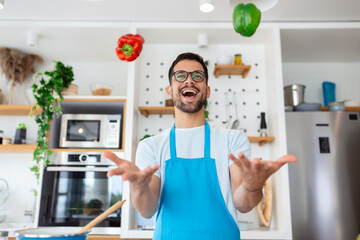 Fototapeta na wymiar Cheerful young man tossing vegetables in air at the kitchen