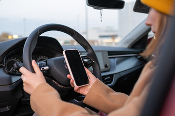 A woman in an orange hat sits at the wheel of a car and uses a mobile phone, side view.