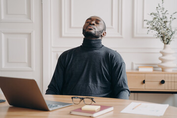 Exhausted home office employee African american male sitting with eyes closed throwing his head back