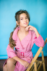 A cute teenage girl with long dark hair in a trendy red plaid raincoat on a blue background in the studio. beauty and fashion
