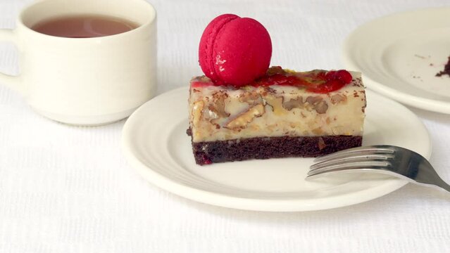 pastry piece slice of cake rectangle shape on white plate and black tea in cup.strawberry cake walnuts orange flower green leaf or pink macaron decoration.fork cutting the desert.tasty morning delight