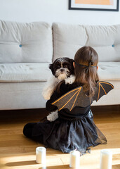 Halloween concept. Girl with a puppy in festive Halloween costumes at home. Back view