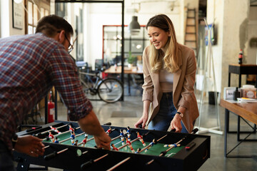 Fototapeta na wymiar Colleagues having fun at work. Businessman and businesswoman playing table soccer