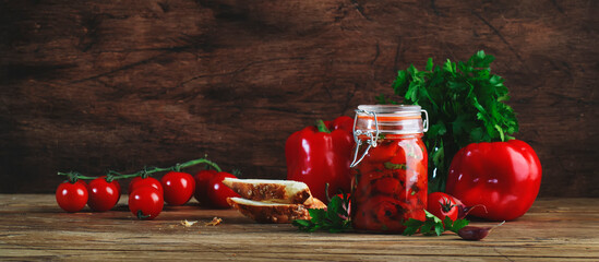 Baked canned red paprika pepper, marinated  with chili, garlic and herbs in glass jar. Rustic wood...