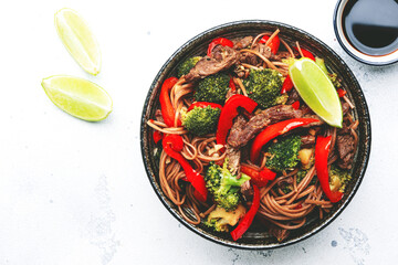 Stir fry noodles with vegetables and beef, paprika and broccoli with sesame seeds in  bowl on white table background, top view