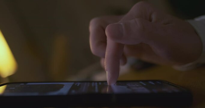 Man's finger flips through a tape of pictures in a smartphone. Side view, close-up, inside a dark room. The end of flipping the tape, removes his hand.