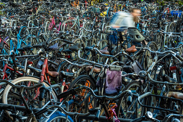 Many bicycles parked chaotically, one cyclist speeding by