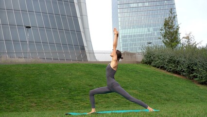 21 year old girl performs yoga gymnastic sport near modern downtown skyscrapers - relax and...