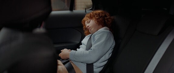 Cute little kid boy sleeping on a back seat of a modern SUV while riding through neighborhood