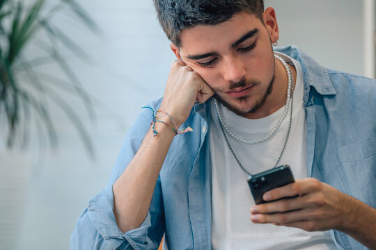 Young Man At Home Looking At Mobile Phone Bored