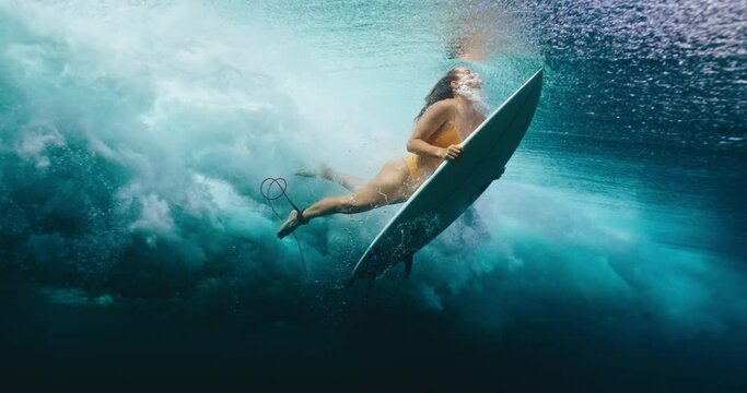 Surfer girl duck dives under large ocean wave, underwater cinematic slow motion
