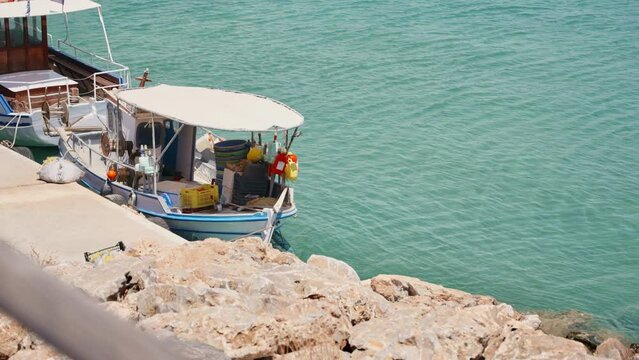 Small fishing boat rocking on sea water tied to a dock in Crete island, Greece. Small sized boat floating in the calm turquoise colored water of Crete. Romantic and beautiful typical Greek scenery