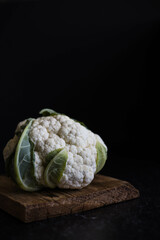 Head of cauliflower on a wooden cutting board on a dark background and side lighting. Close-up.