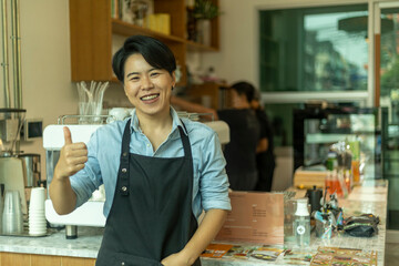 Young LGBT coffee shop owner expresses her gesture with confidence to welcome customer in front of coffee counter