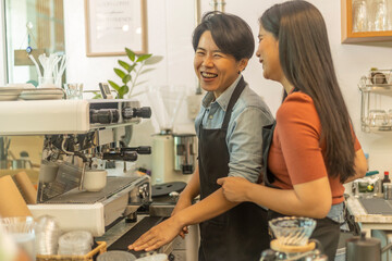 Female business owner works with her LGBT partner to prepare coffee or drink for customer in a coffee shop. A couple of LGBT startup help each other at a coffee counter for their business.