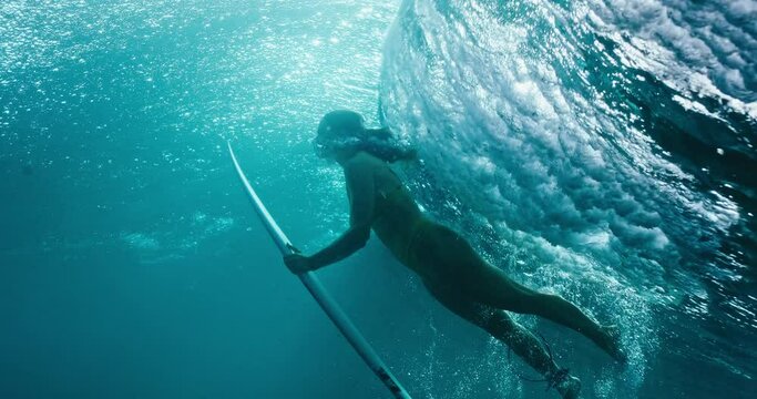 Woman surfer dives below ocean wave, underwater view of surfer girl duck diving, cinematic slow motion shot on RED