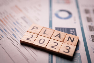 PLAN 2023 text on wooden blocks with the paper report of spreadsheet data analysis graph and charts...