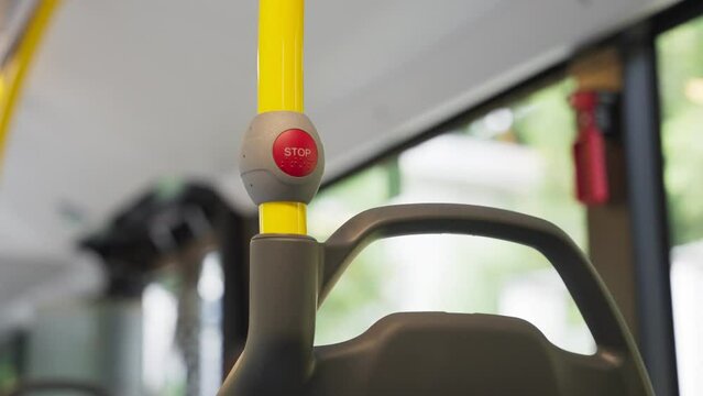 Close up on red stop button on public bus during a ride in the street. European bus driving through city and suburban area. Sign and green trees outside windows. Press to call for a stop in station