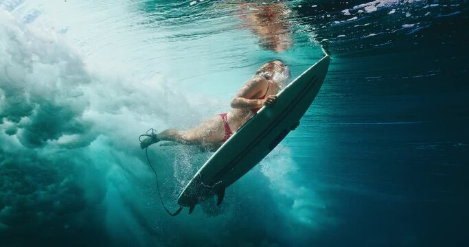 Surfer girl dives under large ocean wave on surfboard, underwater view of woman duck diving