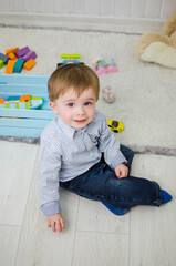Fototapeta premium Boy 2 years old sits on a carpet in a children's room with toys