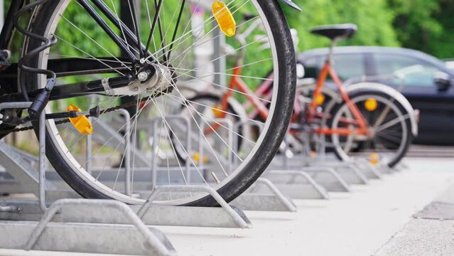 Close up on bicycle wheel tied and parked on bike rack next to railway station. Special racks for transit bikes outside of subway and rail stations. Green way to commute. Safe and trusty parking