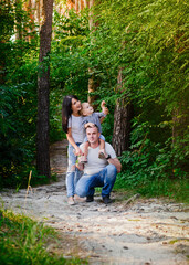 Fototapeta premium Beautiful happy Ukrainian family in the forest in summer. Mom, dad and son 2 years old in the forest.