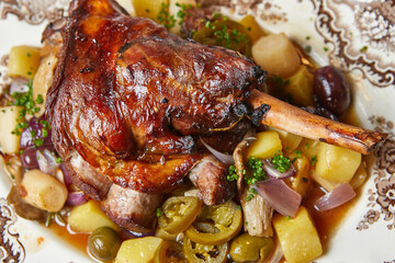 baked duck leg with stewed vegetables in sweet and sour sauce on a plate top view