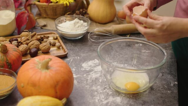 female hands cooking pumpkin pie dough mixing eggs and sugar in bowl with whisk. fall decoration in home kitchen orange pumpkins nuts red leafs foliage. happy thanksgiving day holiday family dinner 