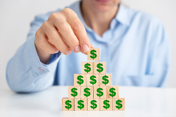 Businesswoman placing wooden block pyramid, dollar signs on wooden blocks