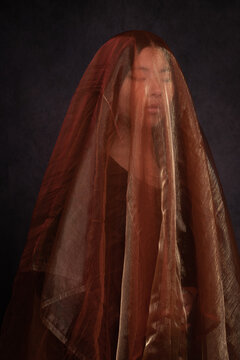 classic dark studo portrait of asian woman in a dress hiding under golden veil	